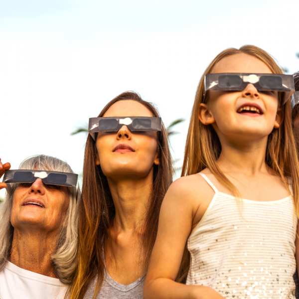 two women and one child wearing eclipse glasses and looking into the sky